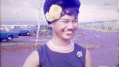 1964: Beehive hairdo happy Asian woman smiles flower in hair.