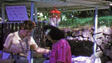 1964: Haole Tourist Woman Receiving Kukui Nut Lei from Native Hawaiian Vendor