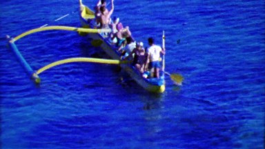 1964: Hawaiian outrigger style boat paddling in bold blue waters.