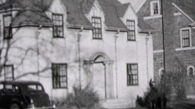 1937: Wealthy suburban white brick house car parked in driveway.