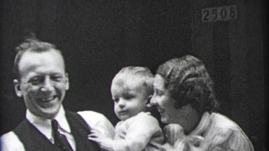 1937: Loving parents laugh with baby in dad's arms.