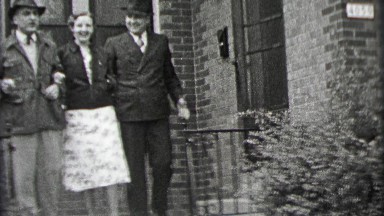 1937: Lady escorted by gentleman doorstep to sidewalk streets.