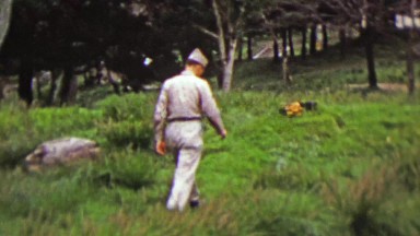 1951: Military soldier hiking in rural green grassy park.