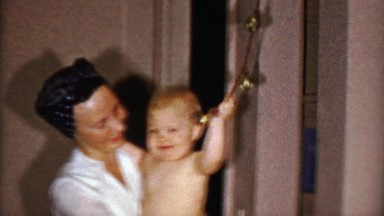 1953: Baby boy ringing bells in Rosie the Riveters style woman arms.