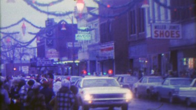 1967: Christmas parade in small downtown city with old timey storefronts.