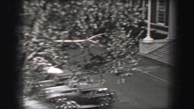 1937: Fancy wealthy cars parked outside collegiate colonnade building entrance.