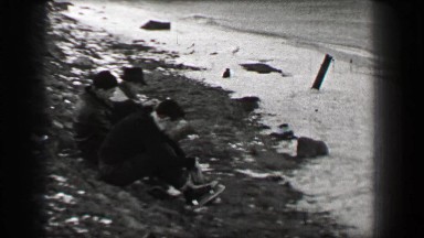 1937: Harvard University students taking off ice skates on frozen river shore.