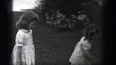 1939: Young girls race over to sit on front porch stoop with wavy curly long