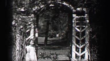 1939: Wealthy young girls play in white formal sundresses under arch garden