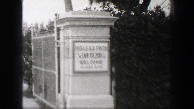 1938: Hialeah Park Visitors Welcome sign entrance palm tree lined street.