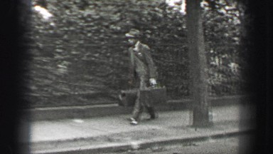 1937: Man crossing street in fedora hat carry leather duffle suitcases. BERLIN,