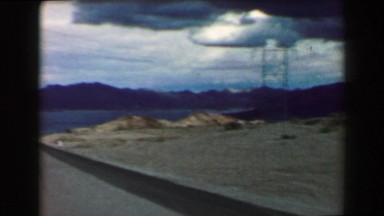1968: Car driving across open space mountainous mirage dry lake ahead. PALM