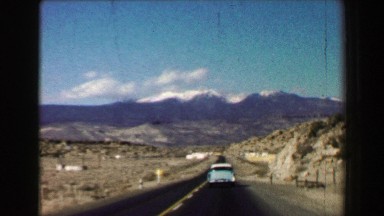 1968: Open road trip travels following 50's classic car snow capped mountains