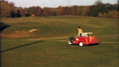 1965: Pre-teen girl practice driving car with golf cart around course. CEDAR