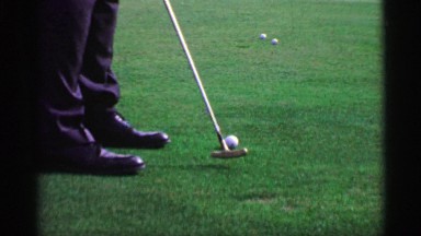1968: Slow motion man putting golf balls on practice green with bullseye putter