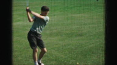 1968: Pre-teen boy hitting golf balls with driver club slow motion swing