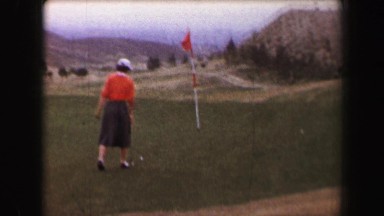 1967: Woman golfer putting on green windy day overlooking hazy valley. PALM