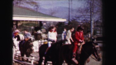 1967: Family riding horses white picket fence stables trotting course. AKRON,