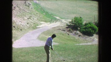 1968: Woman driving golf ball uphill on amazing natural desert landscape course.