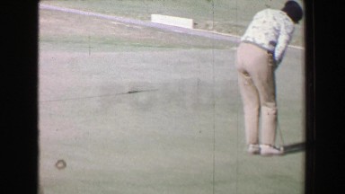 1968: Woman golf putting green mountainous dry Southern California landscape.