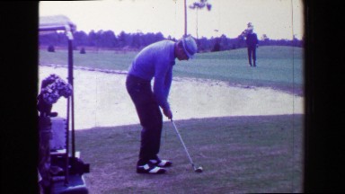 1968: Man pitching golf ball over sand trap onto green close to pin. AMES, IOWA