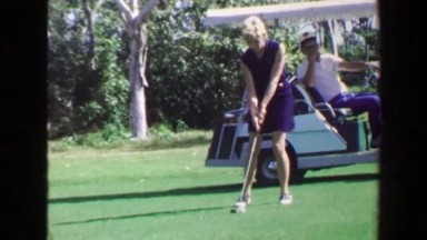 1970: Woman Golfer Hitting 2nd Shot with Man Watching in Power Cart, Ames, Iowa