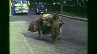 1977: Poor Homeless Man Pulling Cart of Belongings on Busy Streets of Rio