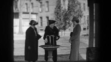 1938: Women filling water bottles from public fountain in formal period dress.