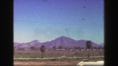 1947: Desert mountain range undeveloped land gravel road car travel palm trees.