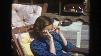1947: Girl sun tanning in blue spotted felt dress basking in summer sunshine.