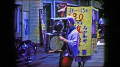 1944: Asian performing artist street clown heavy makeup play drum music.
