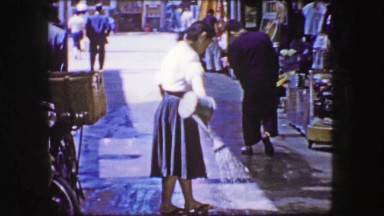 1944: Shopkeeper Watering Hot Sidewalk to Cool Down and Clean Walkway.