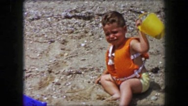 1955: Toddler boy crying at beach meltdown fear scared of ocean water.
