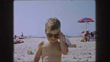 1955: Cool toddler kid wearing Ray Ban wayfarer style sunglasses on white sands