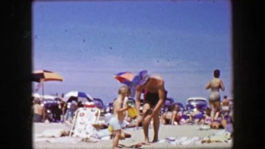 1955: Thin Caucasian Man Taking Toddler Son to Crowded Summertime Beach