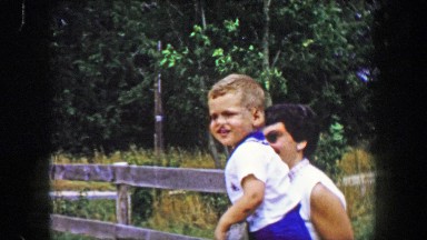 1956: Mother toddler son excitingly watching horses from farm fence.