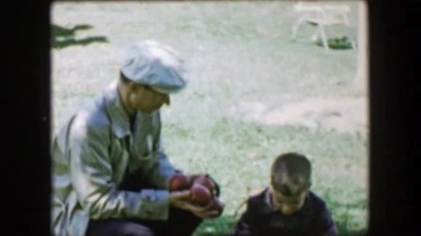 1957: Boy gathering fallen apples giving dad fruit to hold at local food
