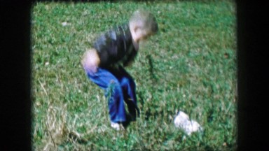 1957: Boy surprised by lost stray cat jumping in long grass petting kitten.