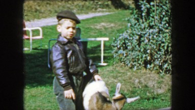 1957: Leather jacket wearing young child petting zoo goat in park.