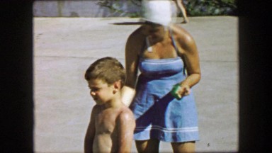 1957: Mother applying suntan lotion on son at public pool before swimming. GLEN,