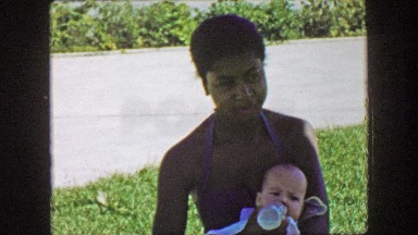 1957: African American black woman feeding caucasian white baby milk bottle.