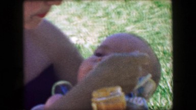 1957: Closeup mother feeding chubby baby boy outdoor summer park chair. GLEN,