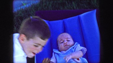 1957: Baby brother puts infant brother on inflatable summer lawn bed. GLEN, NEW