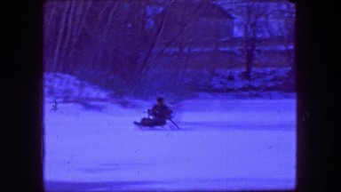 1961: Man driving fan hovercraft over frozen ice pond winter wilderness.