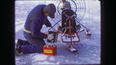 1961: Man maintaining fan hovercraft ski vehicle over winter frozen ice pond.