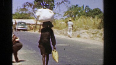 1953: Woman Carries Sack of Laundry on Head Down Middle of Street, San Juan, Puerto Rico