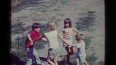 1957: Kids playing ring around the rosie fall down game in country rural
