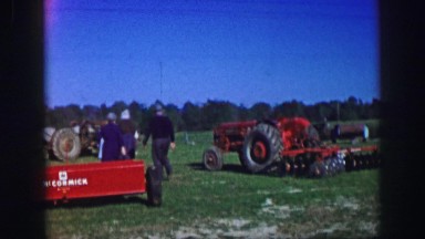 1961: Couple Inspecting Farming Equipment at Rural Yard Sale in Iowa
