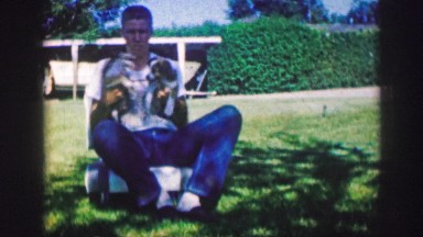 1961: man sitting holding two dogs and then dogs jump down IOWA