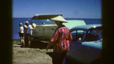 1961: old school car towing a boat to the beach on a hot summer day